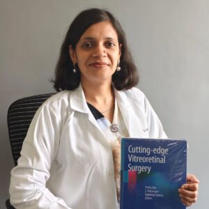 Dr Astha Jain retina surgeon holding her book Cutting Edge Vitreoretinal Surgery at Peepal Eye & Retina Clinic near Chunabhatti